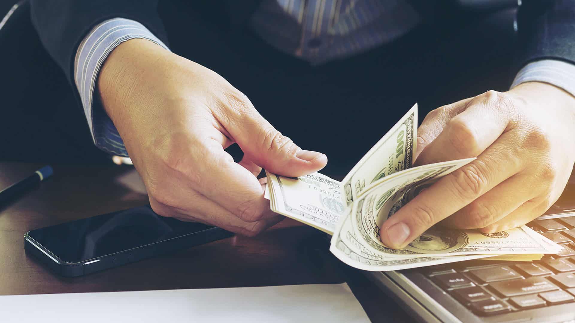 Mains comptant des billets en devises étrangères avec smartphone et clavier en arrière-plan
