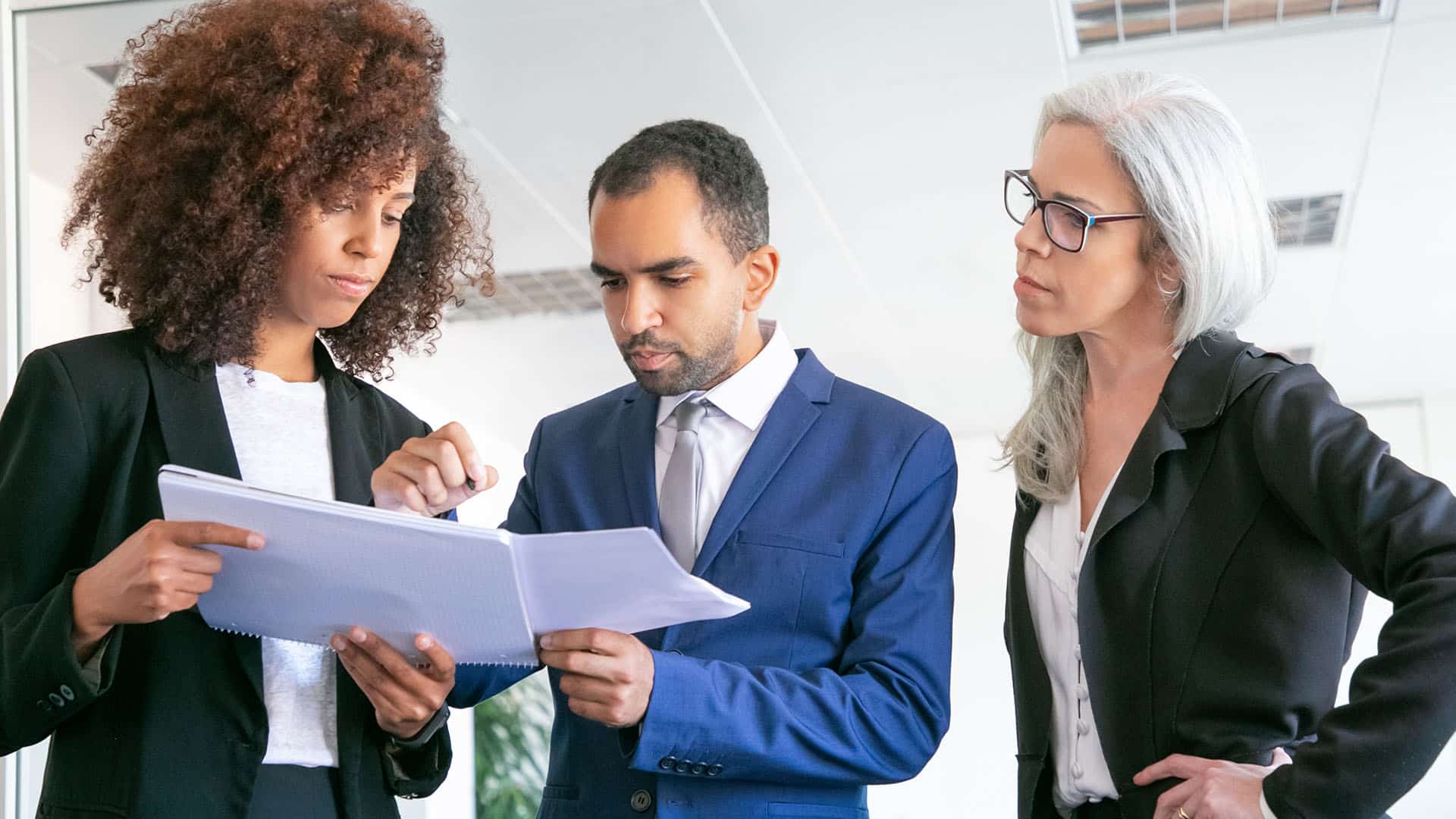 Trois professionnels en costume discutent d'un document en bureau moderne
