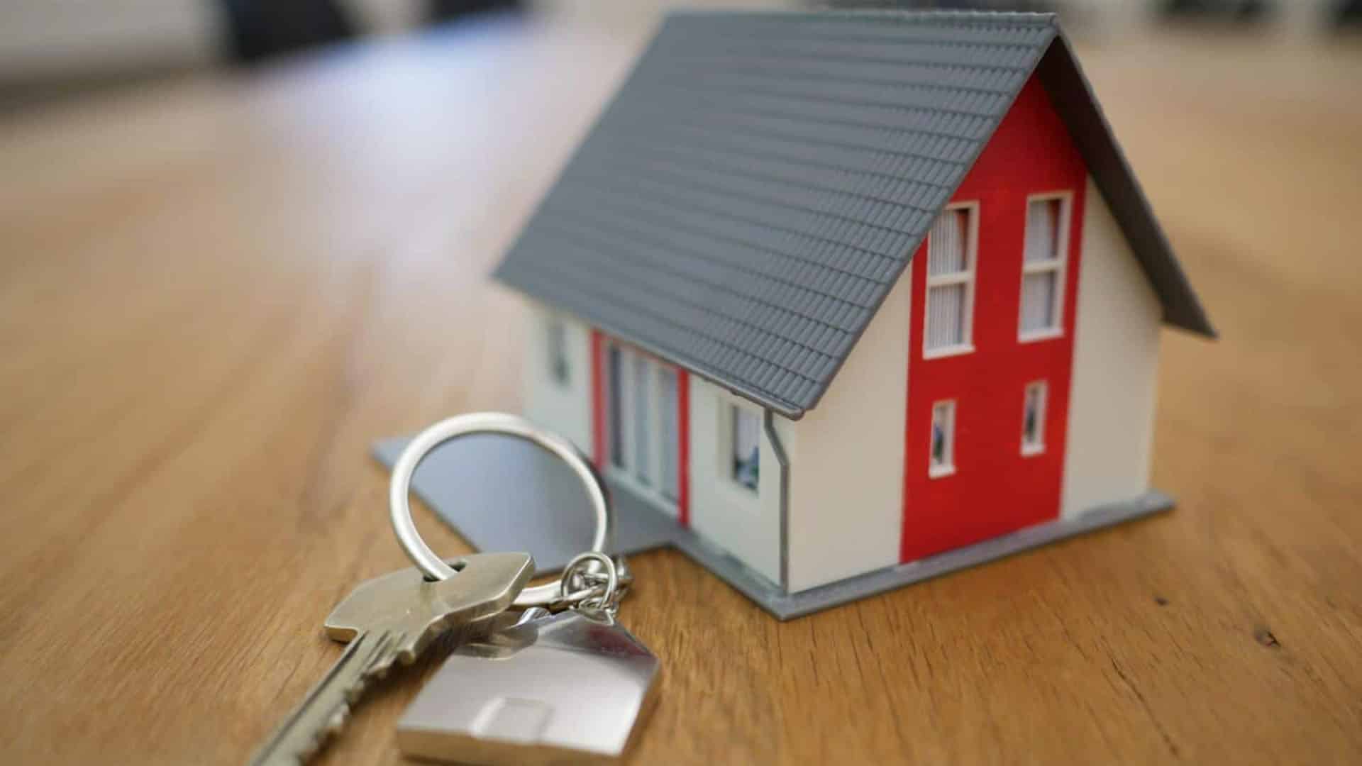 Clé d'argent avec porte-clés maison devant maquette de maison rouge et blanche