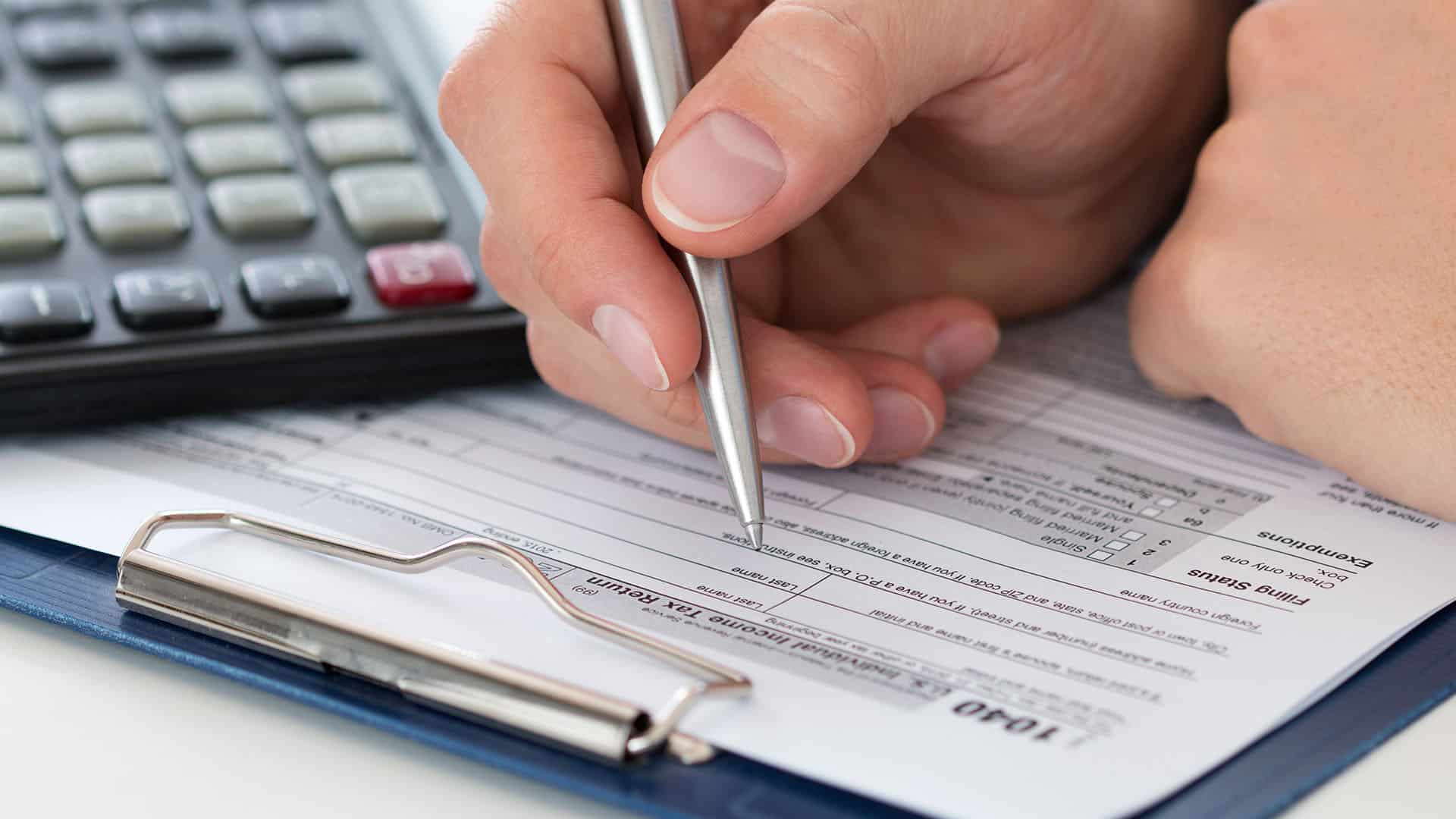 Main tenant un stylo sur un document financier avec calculatrice et bloc-notes en arrière-plan