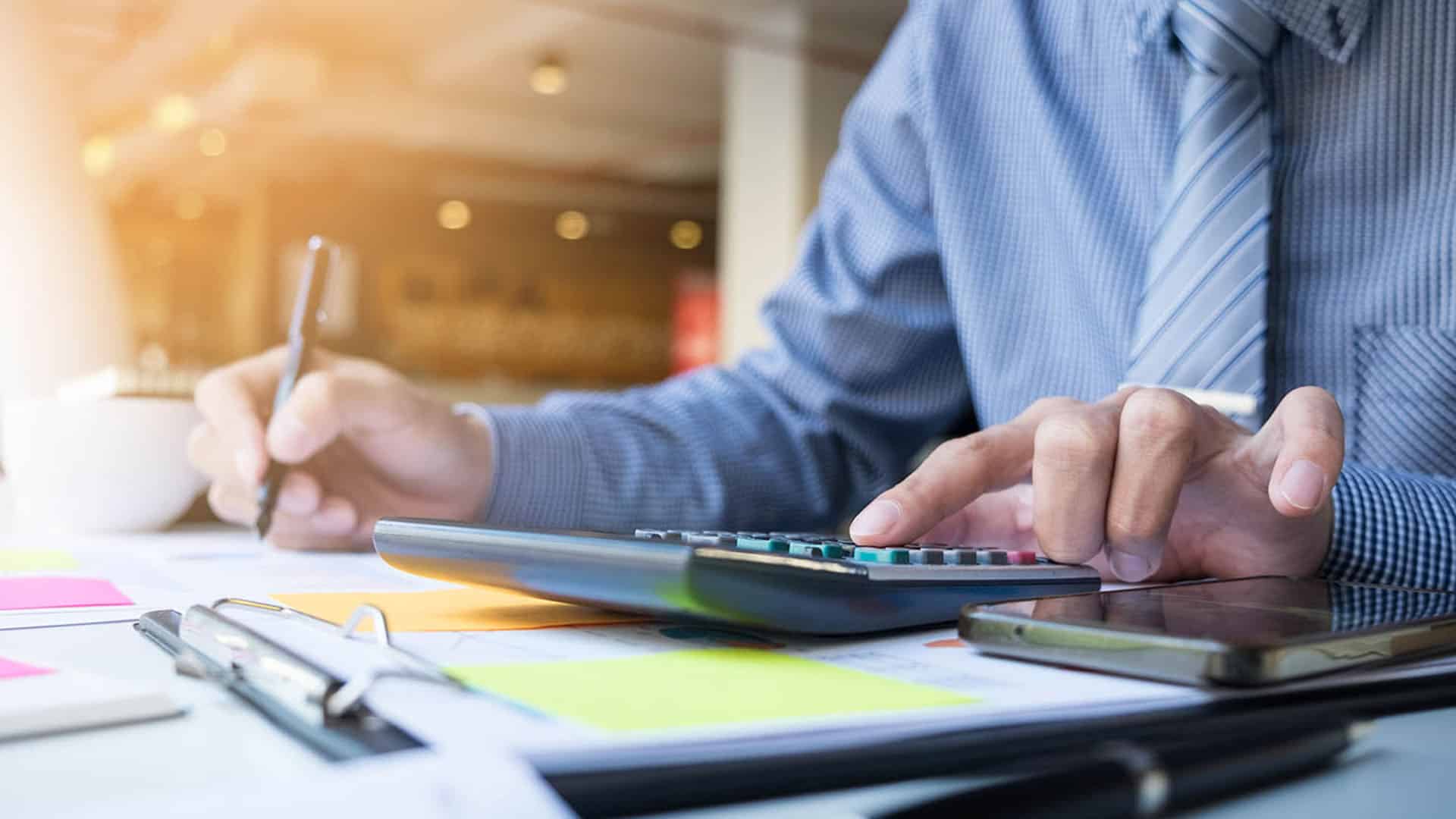 Homme d'affaires en chemise bleue utilisant une calculatrice et un stylo pour des calculs financiers, travail de bureau