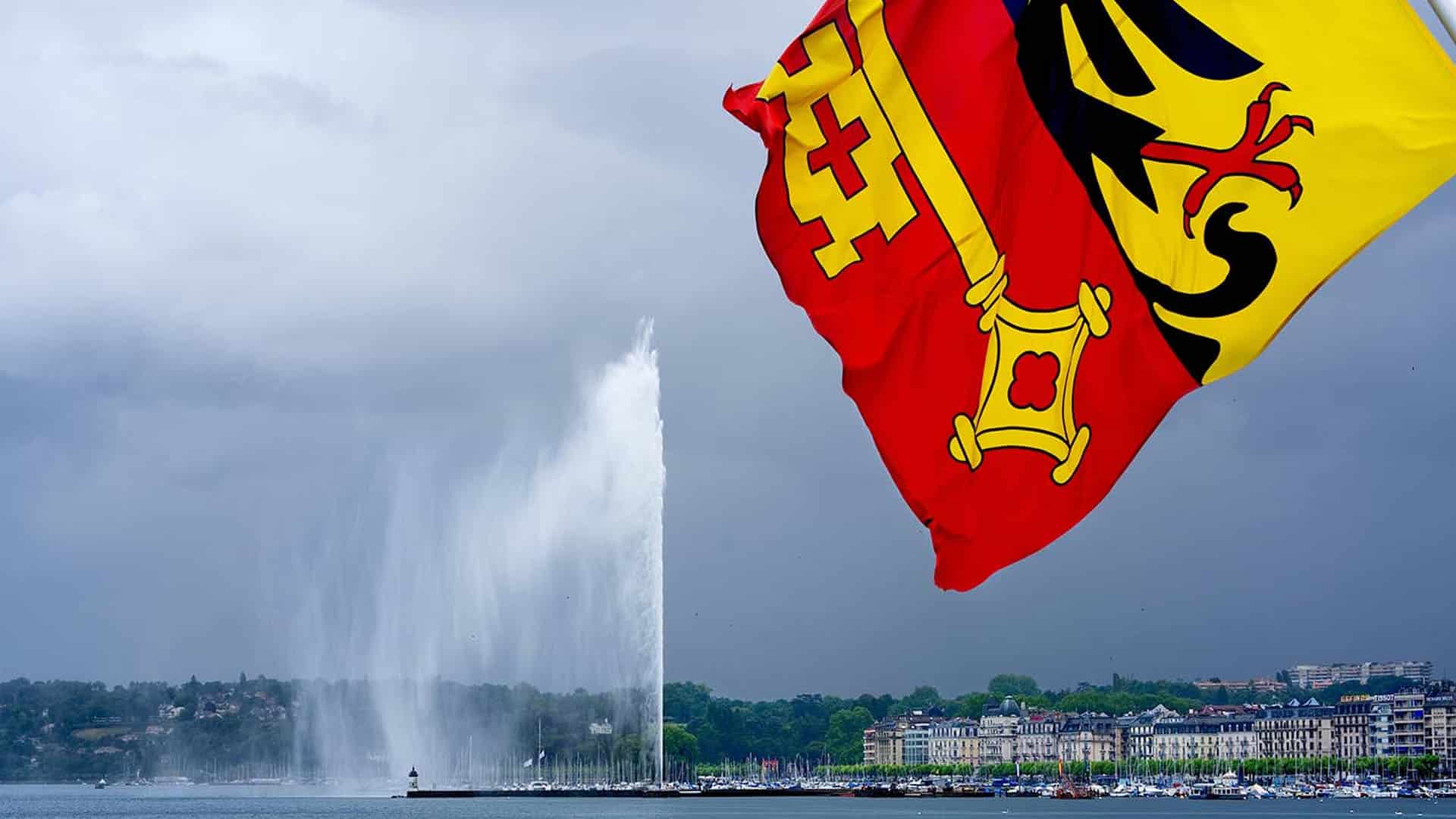 Drapeau suisse avec emblèmes cantonaux flottant au-dessus du Jet d'eau de Genève et du lac Léman