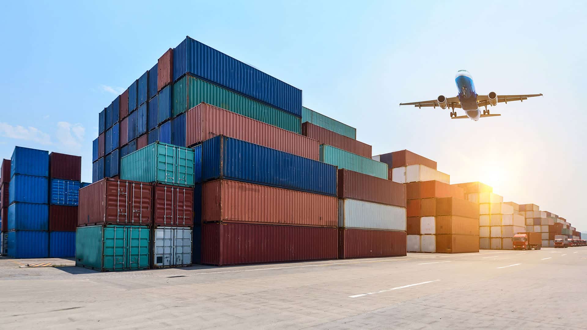 Port avec conteneurs colorés empilés et avion de cargo en approche au coucher de soleil