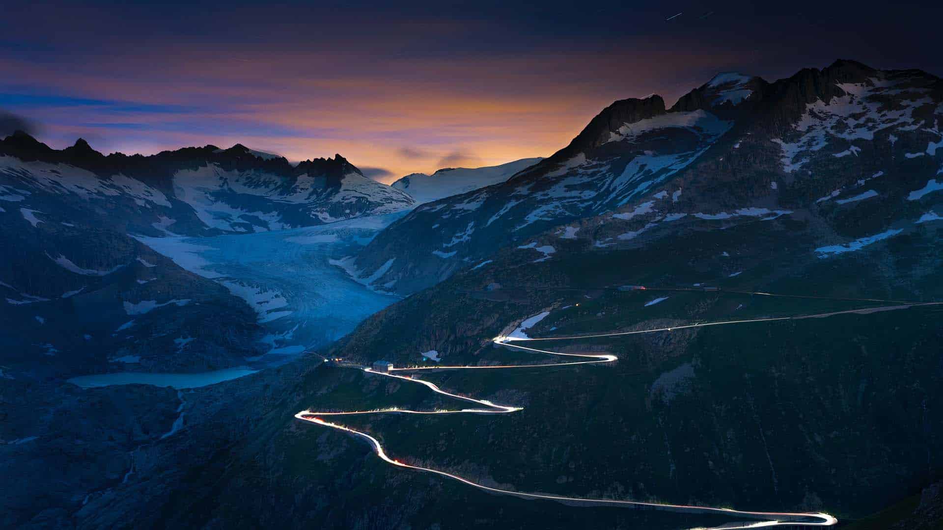 Paysage nocturne des Alpes suisses avec route sinueuse illuminée et montagnes enneigées au crépuscule