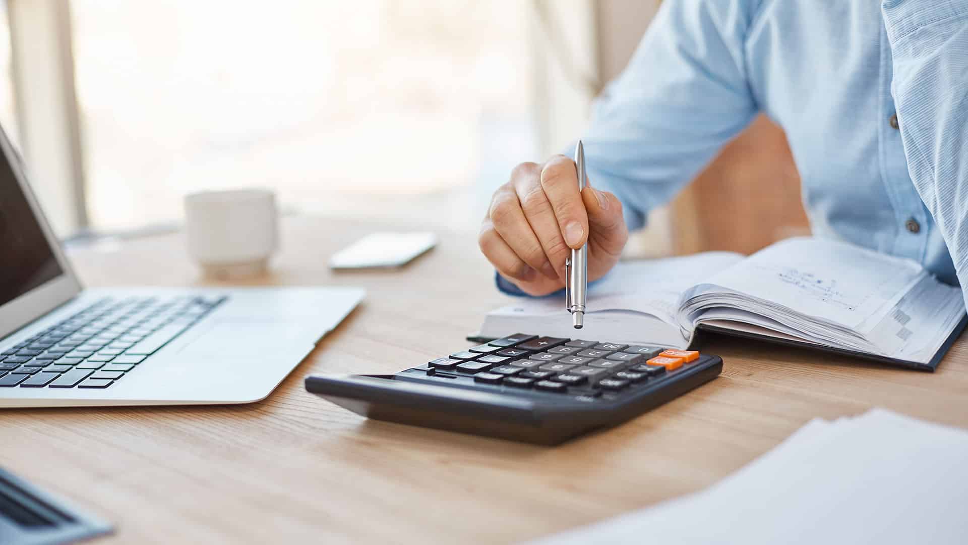 Personne en chemise bleue utilisant une calculatrice et un stylo pour calculer des taux de change CHF EUR