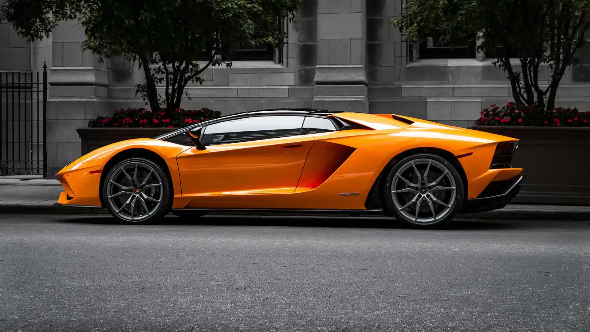 Voiture de luxe orange vif garée devant un bâtiment moderne gris avec végétation