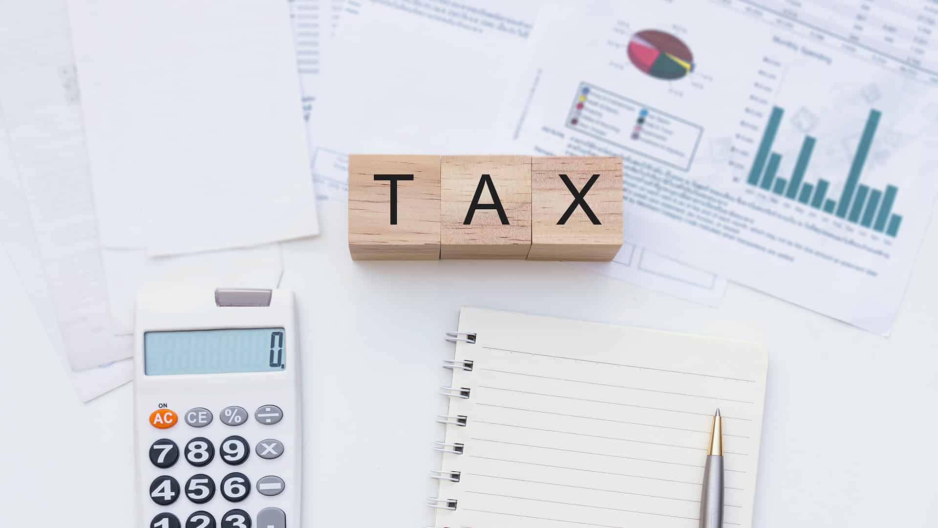 Cubes en bois affichant TAX entourés d'une calculatrice, carnets et graphiques financiers