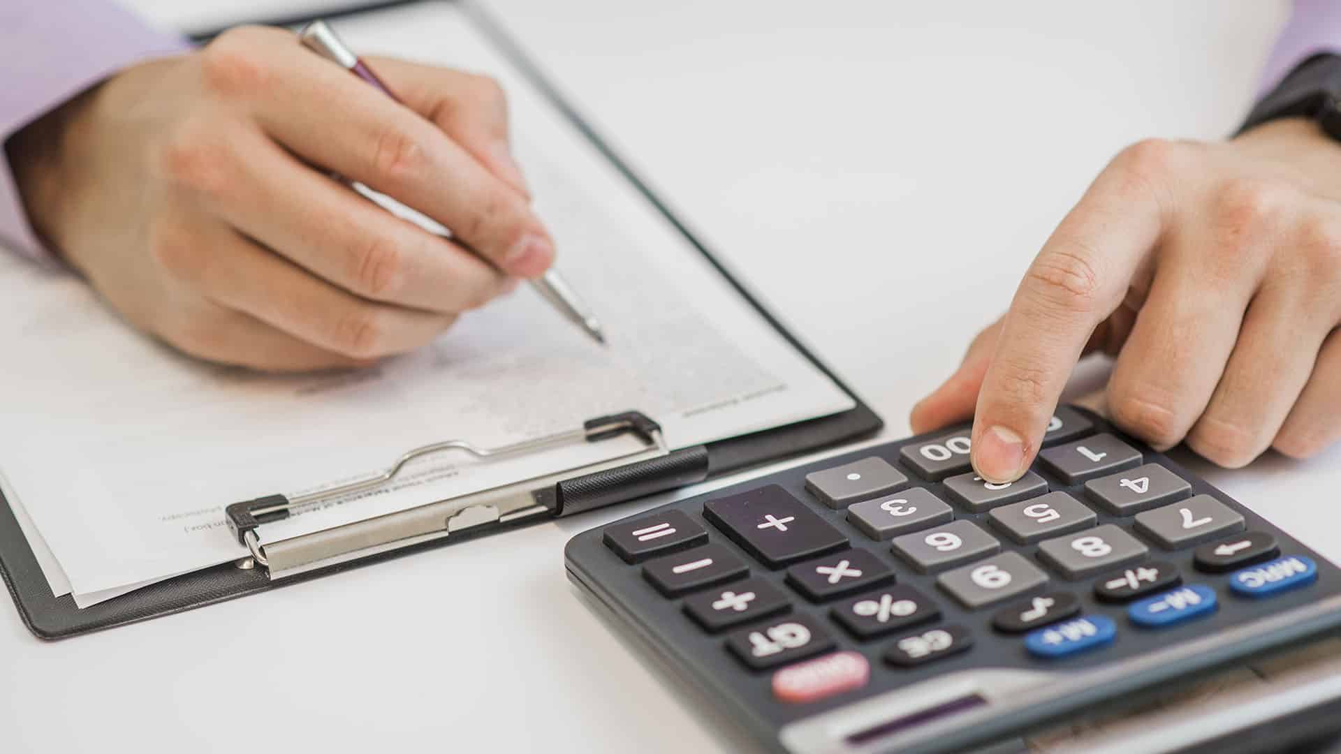 Personne utilisant une calculatrice et écrivant sur un document pour calculer un taux de change CHF EUR