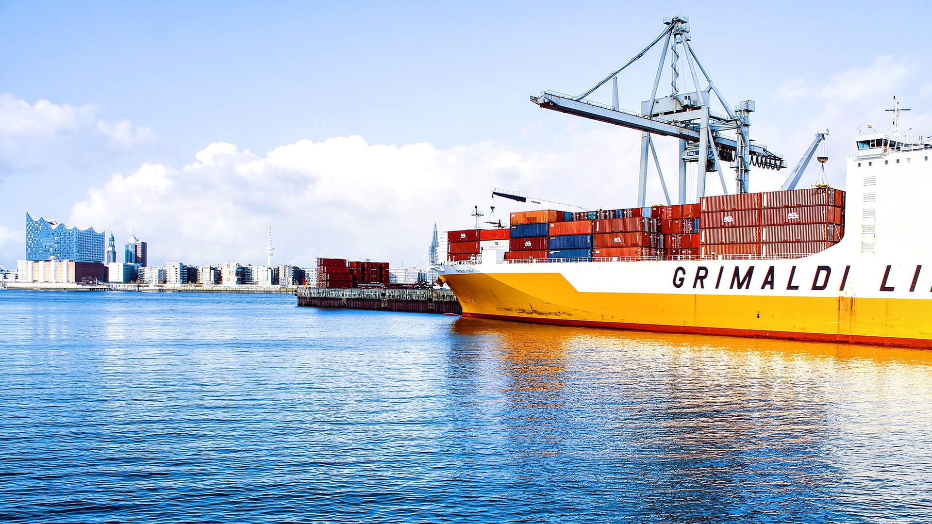 Navire porte-conteneurs jaune et rouge chargeant des conteneurs dans un port international avec grues de manutention