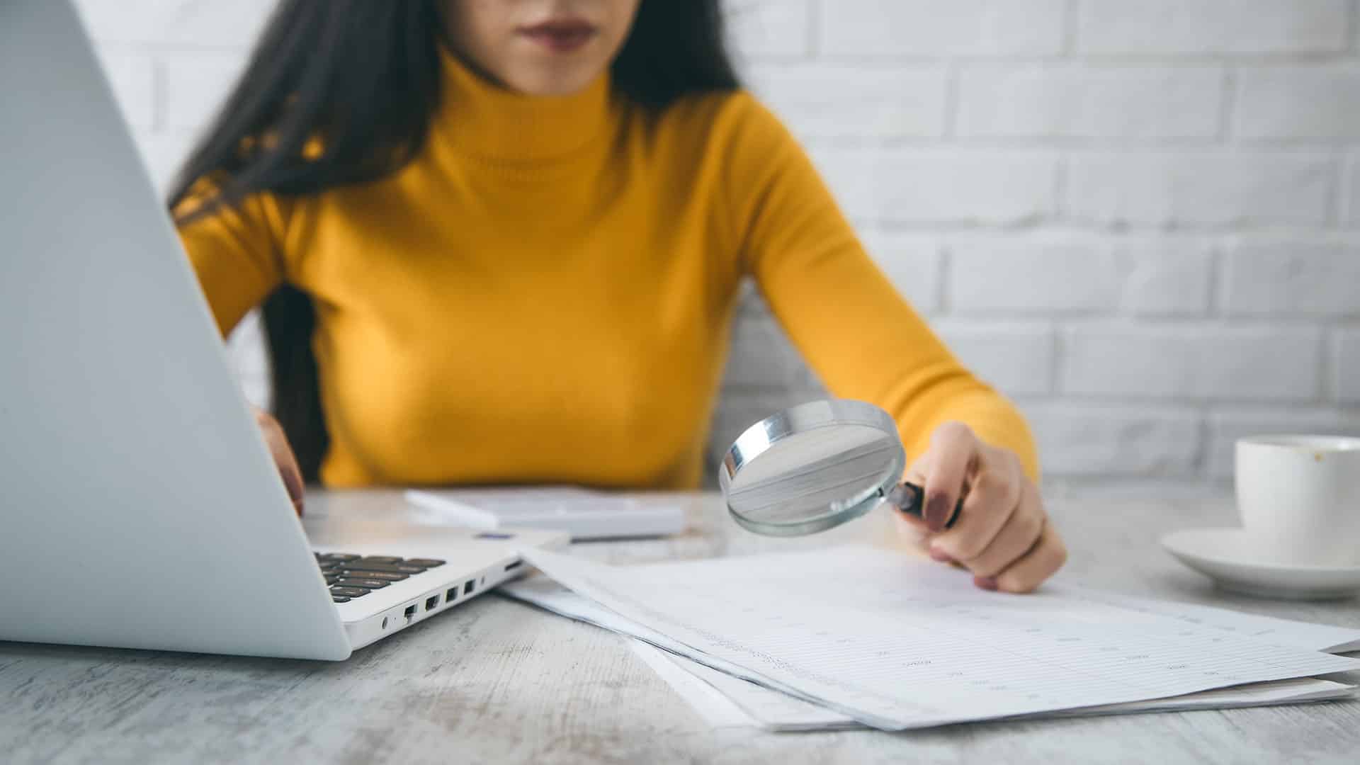 Femme examinant des documents avec loupe, ordinateur portable sur son bureau de travail