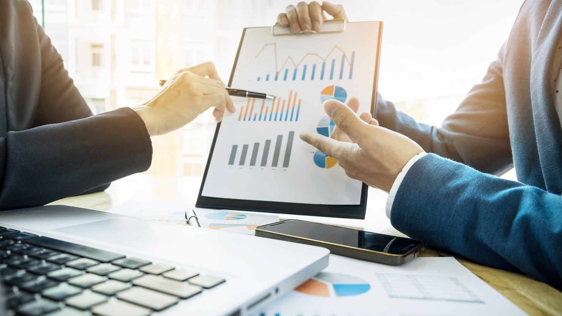 Deux professionnels analysent des graphiques financiers et des diagrammes en camembert lors d'une réunion B2B