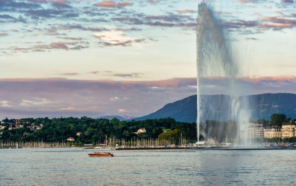 Jet d'eau de Genève avec lac Léman, voiliers et montagnes en arrière-plan au coucher du soleil