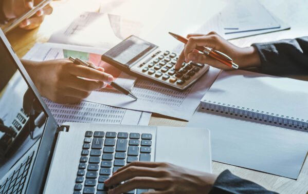 Deux professionnels analysent des données financières avec calculatrice et documents sur un bureau ensoleillé