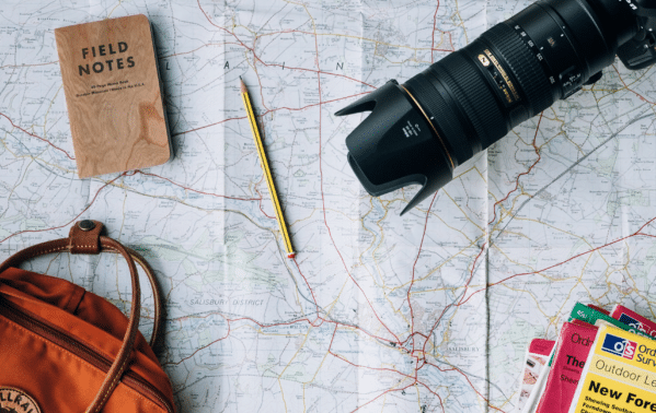 Carnet de voyage, appareil photo, carte routière et accessoires de voyageur sur une table