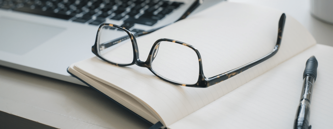 Lunettes de lecture posées sur un carnet ouvert avec ordinateur portable en arrière-plan