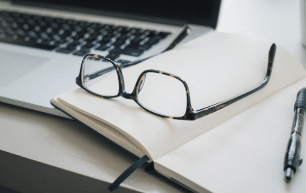 Lunettes de lecture posées sur un carnet ouvert avec ordinateur portable en arrière-plan