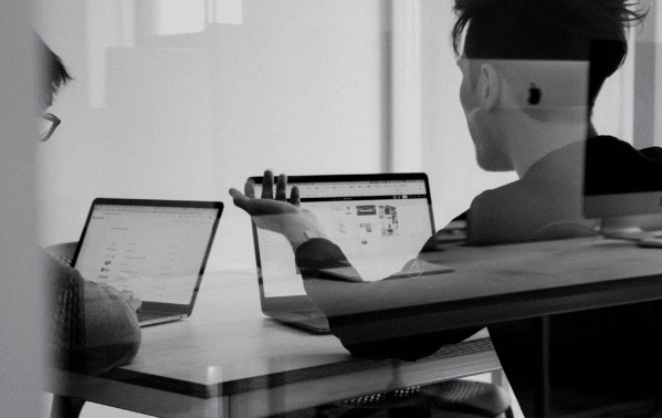 Deux professionnels discutent devant des ordinateurs portables dans un bureau moderne
