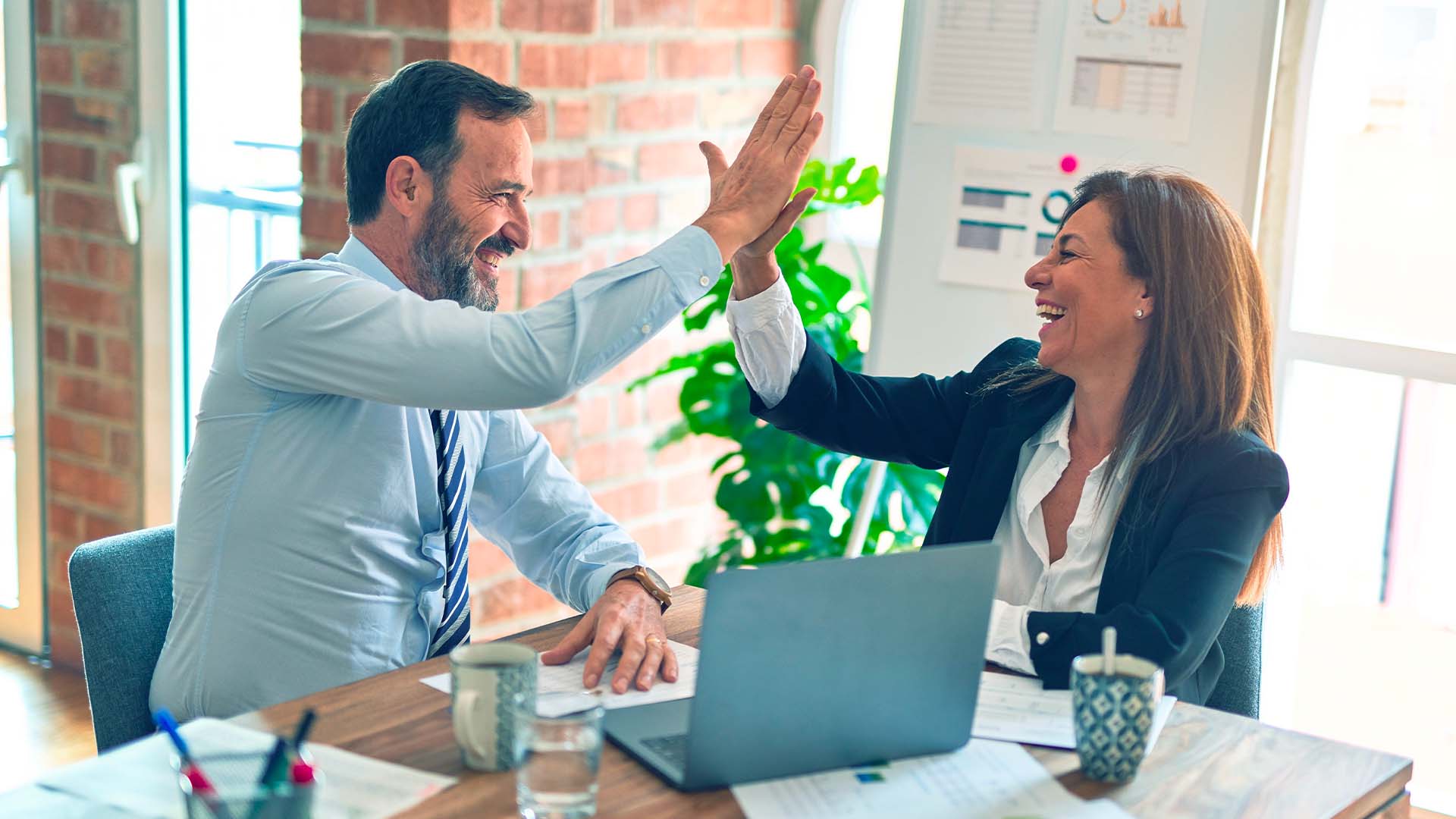 Deux professionnels en tenue d'affaires se donnent un high-five devant un ordinateur portable dans un bureau moderne