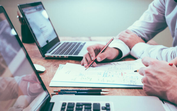 Professionnels en réunion analysant des documents financiers avec ordinateurs et smartphones sur le bureau