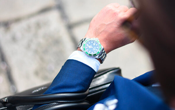 Homme portant montre de luxe avec cadran bleu et costume bleu marine tenant documents financiers