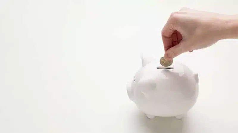 Main déposant une pièce de monnaie dans une tirelire blanche pour symboliser l'épargne et les économies