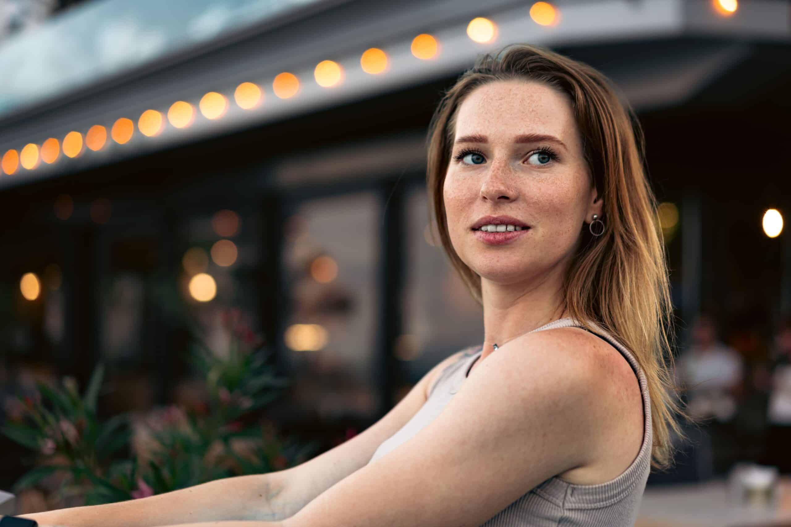 Femme souriante devant un établissement moderne avec lumières ambrées, symbolisant la confiance et la sérénité