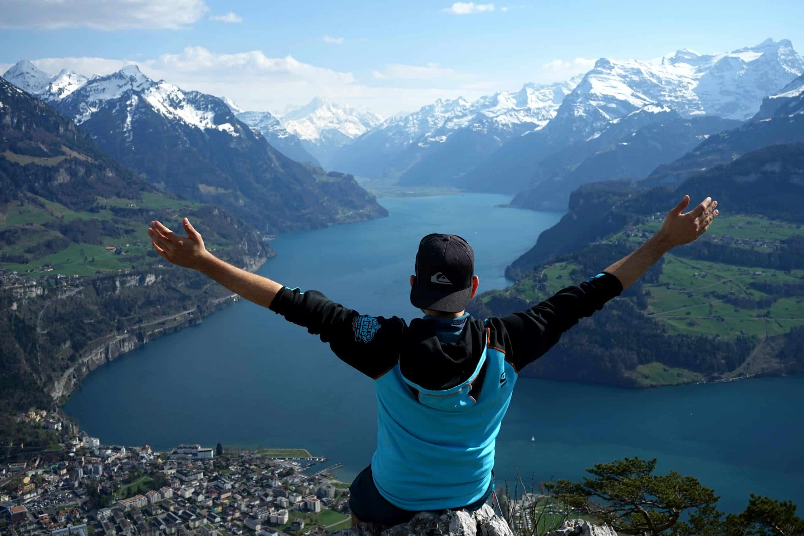 Blick auf einen See und die Schweizer Alpen, mit einem Wanderer von hinten im Vordergrund.